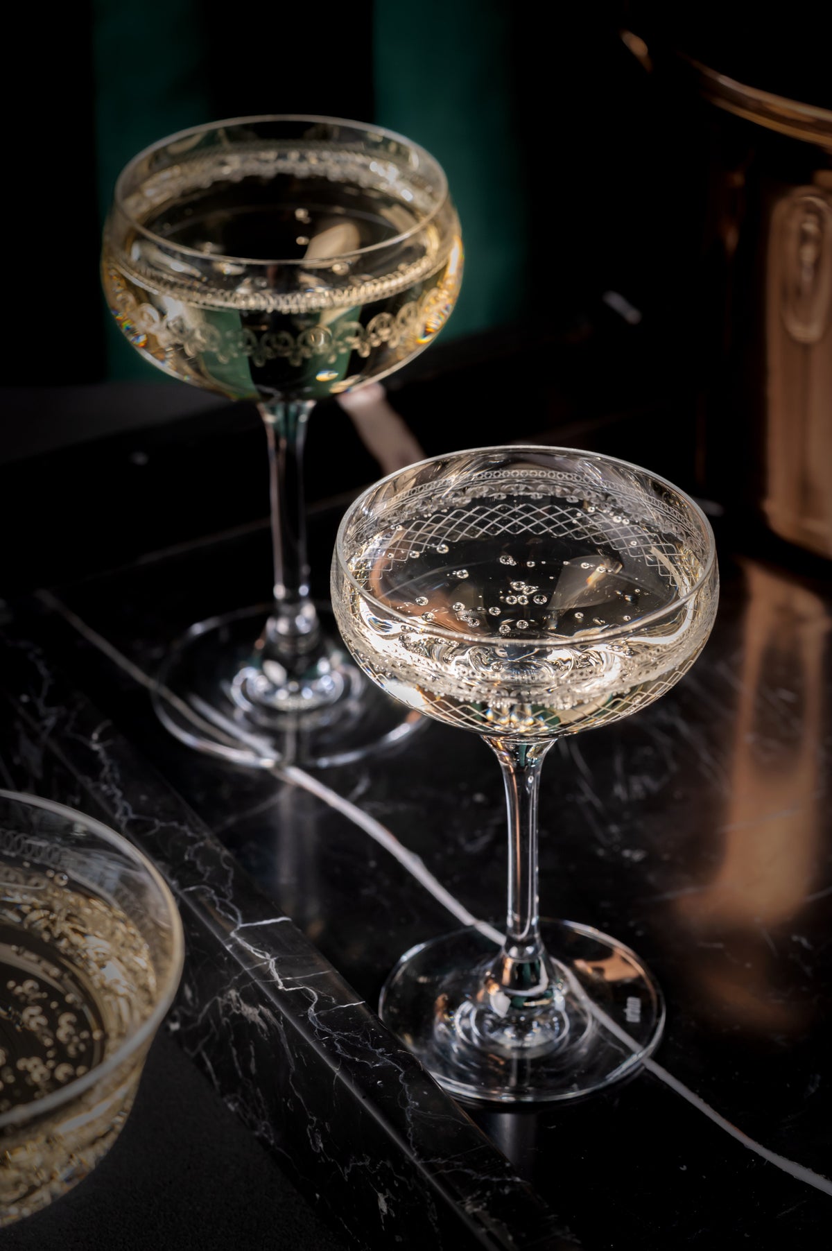 Urban Bar etched coupe glasses with champagne, styled against a dark marble bar with emerald green backdrop and copper bar accessories.